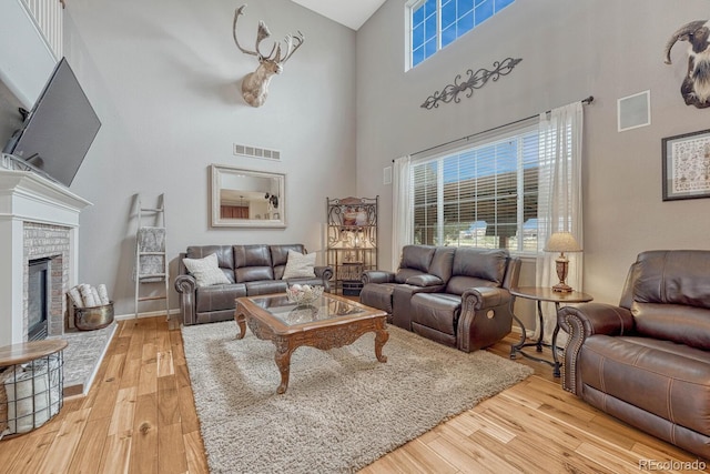 living room with a towering ceiling, light hardwood / wood-style floors, and a brick fireplace