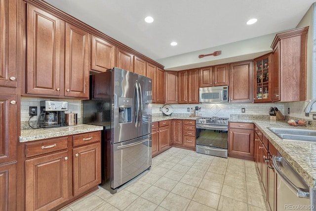 kitchen featuring tasteful backsplash, light tile patterned flooring, appliances with stainless steel finishes, light stone countertops, and sink