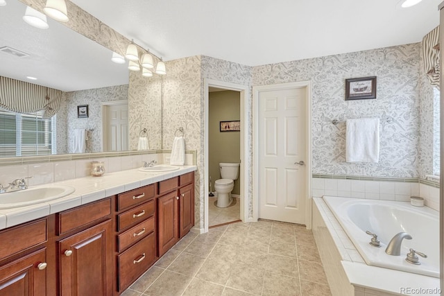 bathroom featuring tile patterned floors, dual bowl vanity, a relaxing tiled tub, and toilet