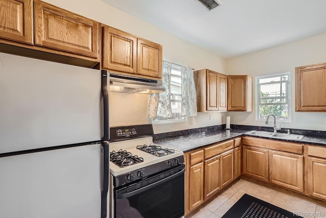 kitchen with light tile patterned floors, gas range oven, white refrigerator, and a healthy amount of sunlight