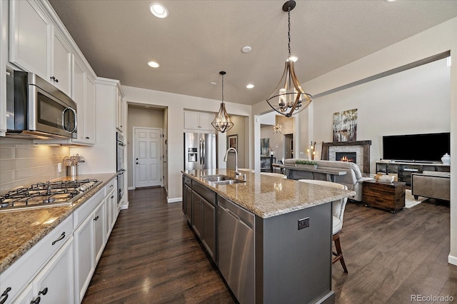 12590 Valentia St, Thornton, CO 80602 - kitchen with a sink, appliances with stainless steel finishes, a lit fireplace, white cabinetry, and dark wood-style flooring