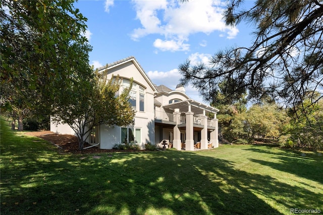 back of house with a yard, a chimney, stucco siding, and a balcony