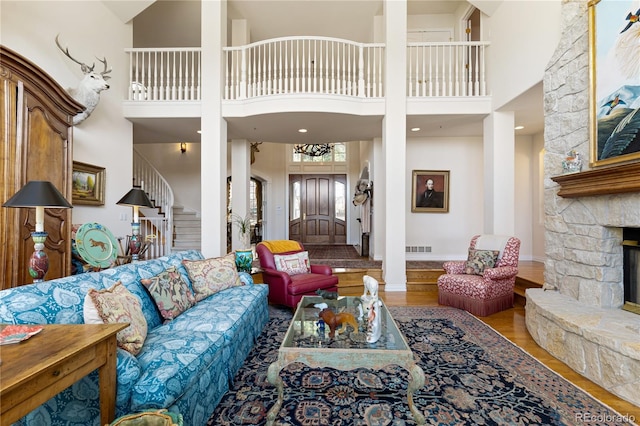living room with wood finished floors, a high ceiling, stairway, visible vents, and a stone fireplace