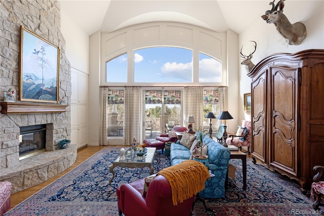 living area featuring a stone fireplace, high vaulted ceiling, and wood finished floors
