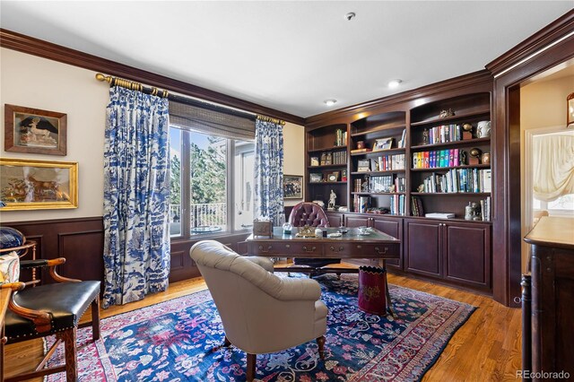 home office featuring a wainscoted wall, crown molding, light wood-type flooring, and built in features