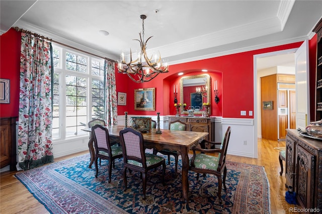 dining space featuring a wainscoted wall, light wood-type flooring, an inviting chandelier, crown molding, and arched walkways