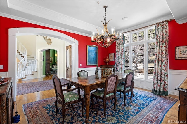 dining space with an inviting chandelier, wood finished floors, crown molding, arched walkways, and stairs