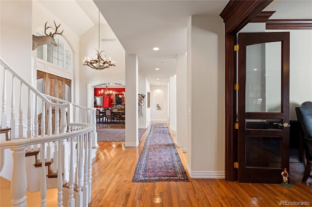foyer featuring light wood finished floors, a notable chandelier, visible vents, baseboards, and stairway