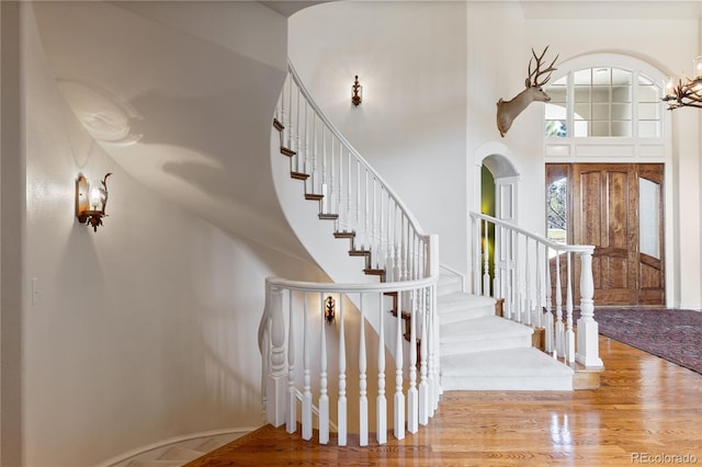 foyer with stairway, wood finished floors, a high ceiling, and a notable chandelier