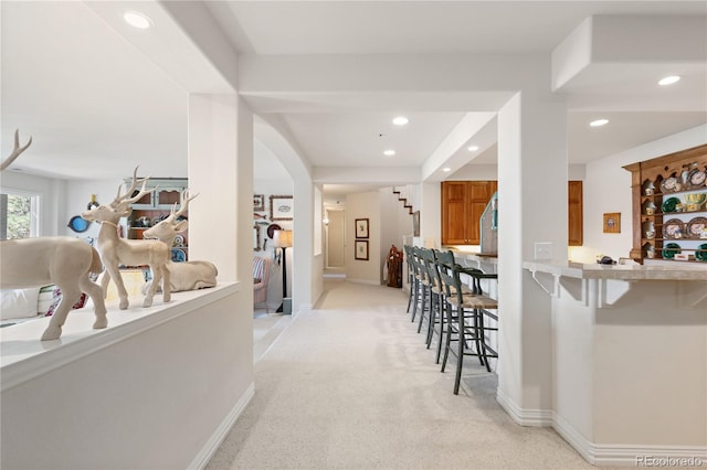 corridor featuring light colored carpet, baseboards, arched walkways, and stairs