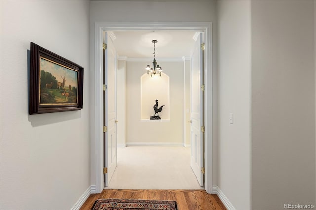 corridor with baseboards, an inviting chandelier, light wood-style flooring, and crown molding