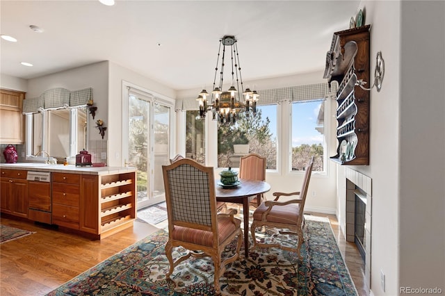 dining space featuring an inviting chandelier, light wood-style floors, a tiled fireplace, and a healthy amount of sunlight