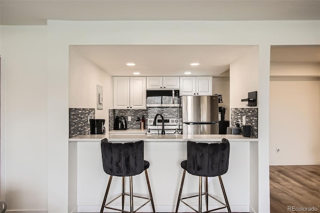 kitchen featuring freestanding refrigerator, a breakfast bar, a sink, a peninsula, and decorative backsplash