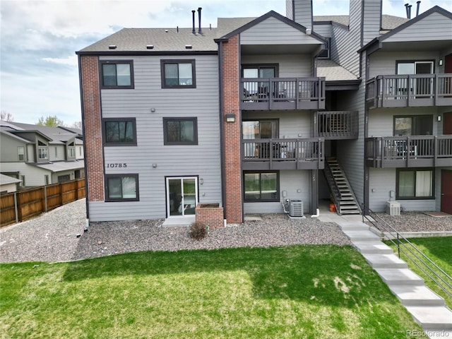 back of property featuring a lawn, brick siding, fence, stairs, and central AC unit