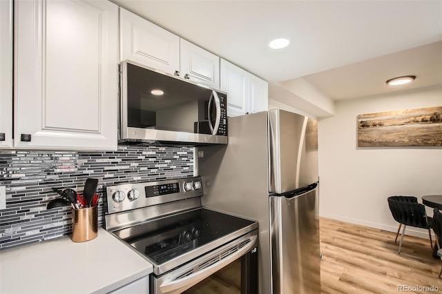 kitchen featuring light wood-style flooring, stainless steel appliances, white cabinetry, light countertops, and decorative backsplash