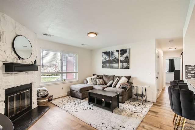 living area featuring a fireplace, baseboards, visible vents, and wood finished floors