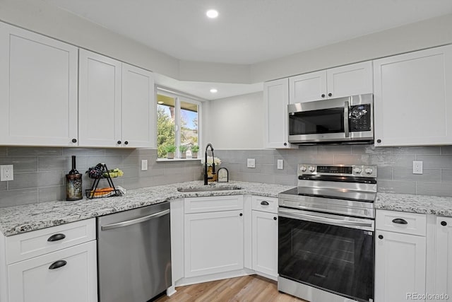 kitchen with stainless steel appliances, a sink, white cabinets, light wood-style floors, and tasteful backsplash