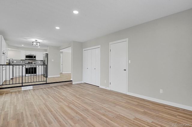 unfurnished living room with recessed lighting, baseboards, light wood finished floors, and a sink