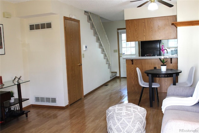 living room with stairway, visible vents, ceiling fan, and wood finished floors