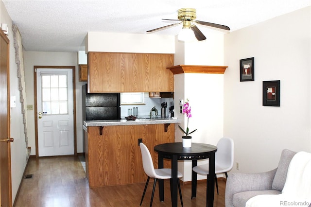 kitchen featuring freestanding refrigerator, ceiling fan, a peninsula, brown cabinets, and light wood finished floors
