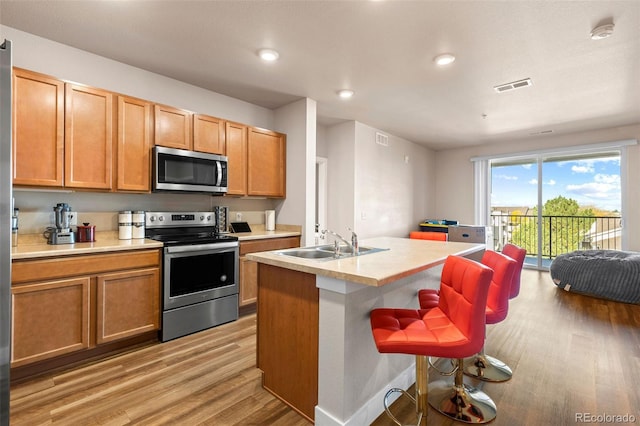 kitchen with sink, light wood-type flooring, a kitchen breakfast bar, stainless steel appliances, and a center island with sink