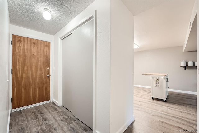 hallway with a textured ceiling and light hardwood / wood-style flooring