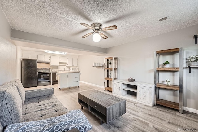 living room with ceiling fan, light wood-type flooring, sink, and a textured ceiling