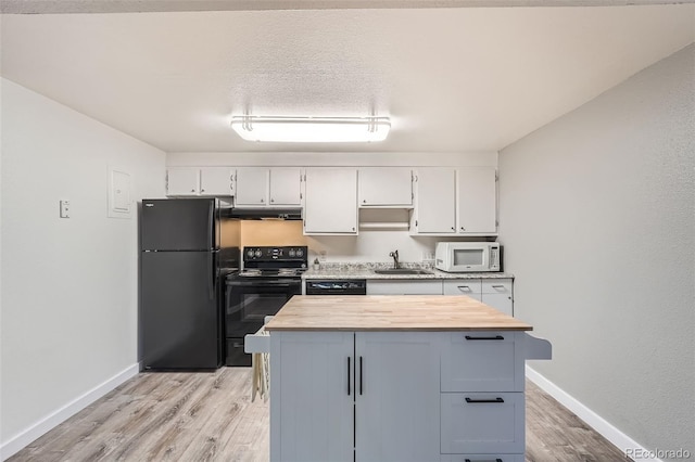 kitchen with a textured ceiling, light hardwood / wood-style flooring, black appliances, wood counters, and sink