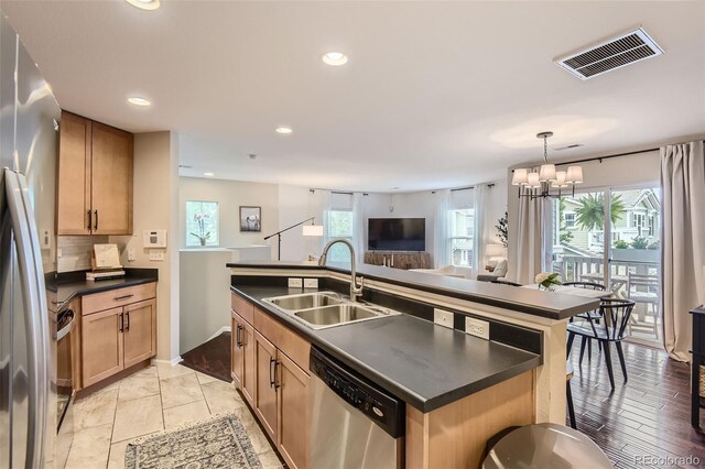 kitchen with a center island with sink, sink, appliances with stainless steel finishes, a healthy amount of sunlight, and a chandelier