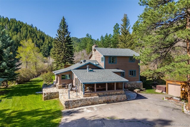 11531 S Deer Creek Rd, Littleton, CO 80127 - back of property with a forest view, a chimney, a shingled roof, a yard, and stone siding