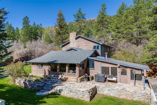 11531 S Deer Creek Rd, Littleton, CO 80127 - back of house with a chimney, a patio area, a forest view, a shingled roof, and a lawn