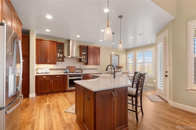 kitchen featuring pendant lighting, a center island with sink, wall chimney range hood, sink, and stainless steel appliances