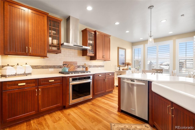 kitchen with decorative backsplash, light wood-type flooring, wall chimney exhaust hood, stainless steel appliances, and pendant lighting