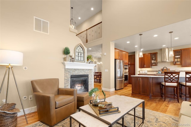 living room featuring a fireplace, a towering ceiling, light hardwood / wood-style floors, and sink