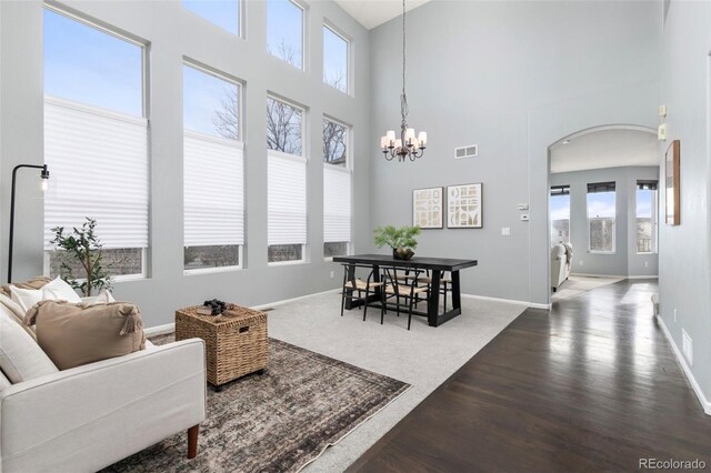 living room with dark wood-style floors, arched walkways, visible vents, an inviting chandelier, and baseboards