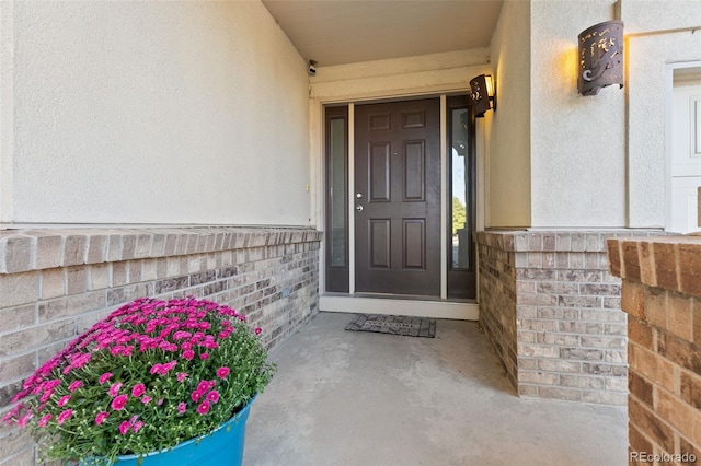 view of exterior entry featuring brick siding and stucco siding