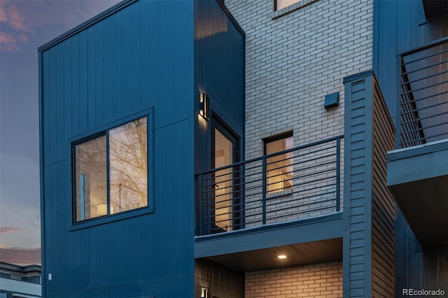 property exterior at dusk with brick siding and a balcony