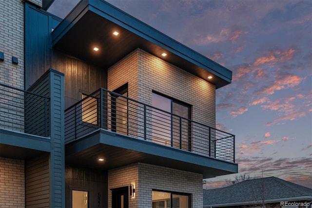 property exterior at dusk with a balcony and brick siding