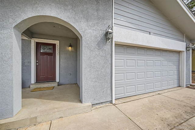 entrance to property featuring a garage, concrete driveway, and stucco siding