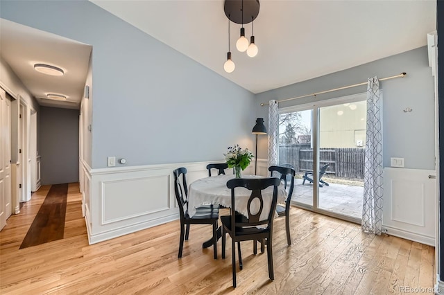 dining space featuring lofted ceiling, a decorative wall, light wood-style floors, and wainscoting