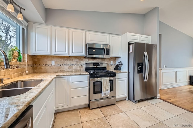 kitchen featuring backsplash, lofted ceiling, appliances with stainless steel finishes, light tile patterned flooring, and a sink