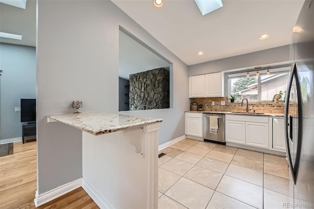 kitchen with light stone countertops, a sink, stainless steel appliances, white cabinets, and backsplash