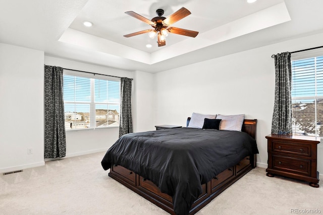 bedroom featuring light colored carpet, a raised ceiling, and ceiling fan