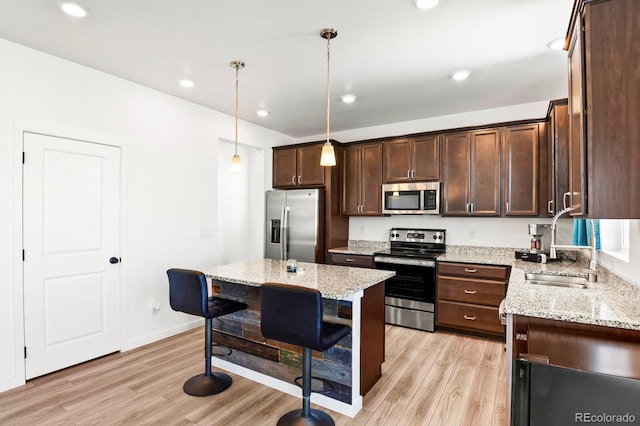 kitchen with light stone counters, stainless steel appliances, pendant lighting, light hardwood / wood-style floors, and a kitchen island