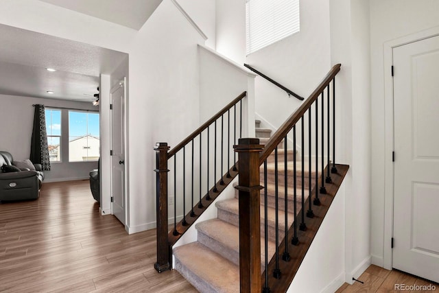 staircase with ceiling fan, a textured ceiling, and hardwood / wood-style flooring