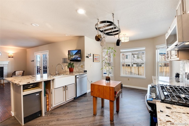 kitchen featuring sink, dark wood-type flooring, light stone counters, a tiled fireplace, and stainless steel dishwasher