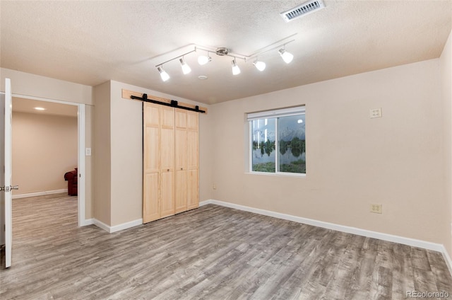 unfurnished bedroom featuring hardwood / wood-style flooring, a barn door, a closet, and a textured ceiling