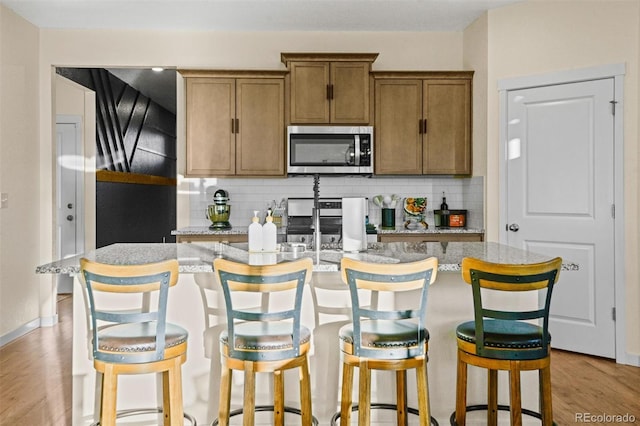 kitchen featuring light wood-type flooring, backsplash, stainless steel appliances, a breakfast bar, and a center island with sink