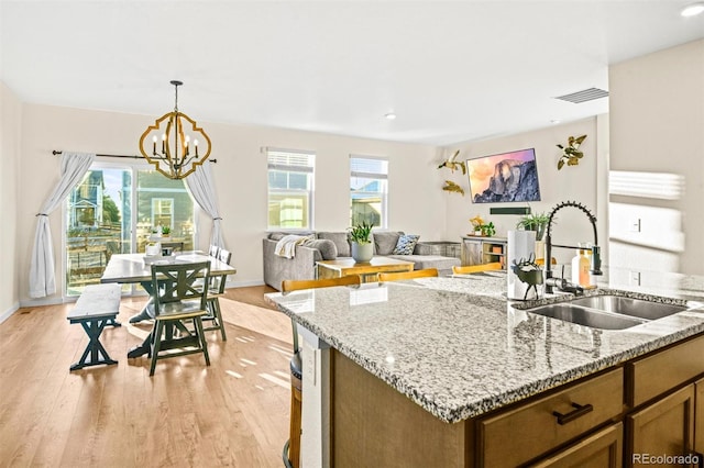 kitchen featuring light hardwood / wood-style flooring, sink, pendant lighting, a chandelier, and light stone counters