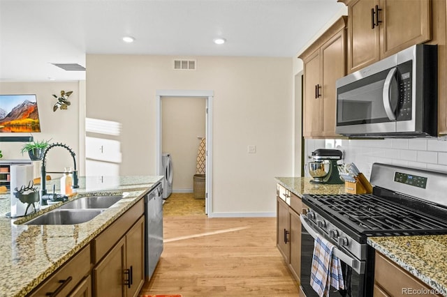 kitchen with stainless steel appliances, backsplash, sink, light wood-type flooring, and light stone counters